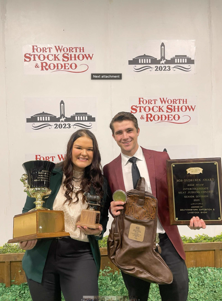 Zach Holescher and one other person holding up awards with a sign in the background that reads "Fort Worth Stockshow and Rodeo".
